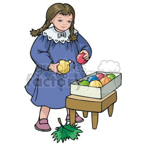 The clipart image features a young girl in a blue dress with a white collar, holding a yellow Christmas bulb in one hand and a red one in the other. She is standing next to a small table or stool which has a box containing colorful Christmas ornaments. There is also a green piece of what appears to be Christmas tree foliage or a holly leaf on the ground near the girl's feet.